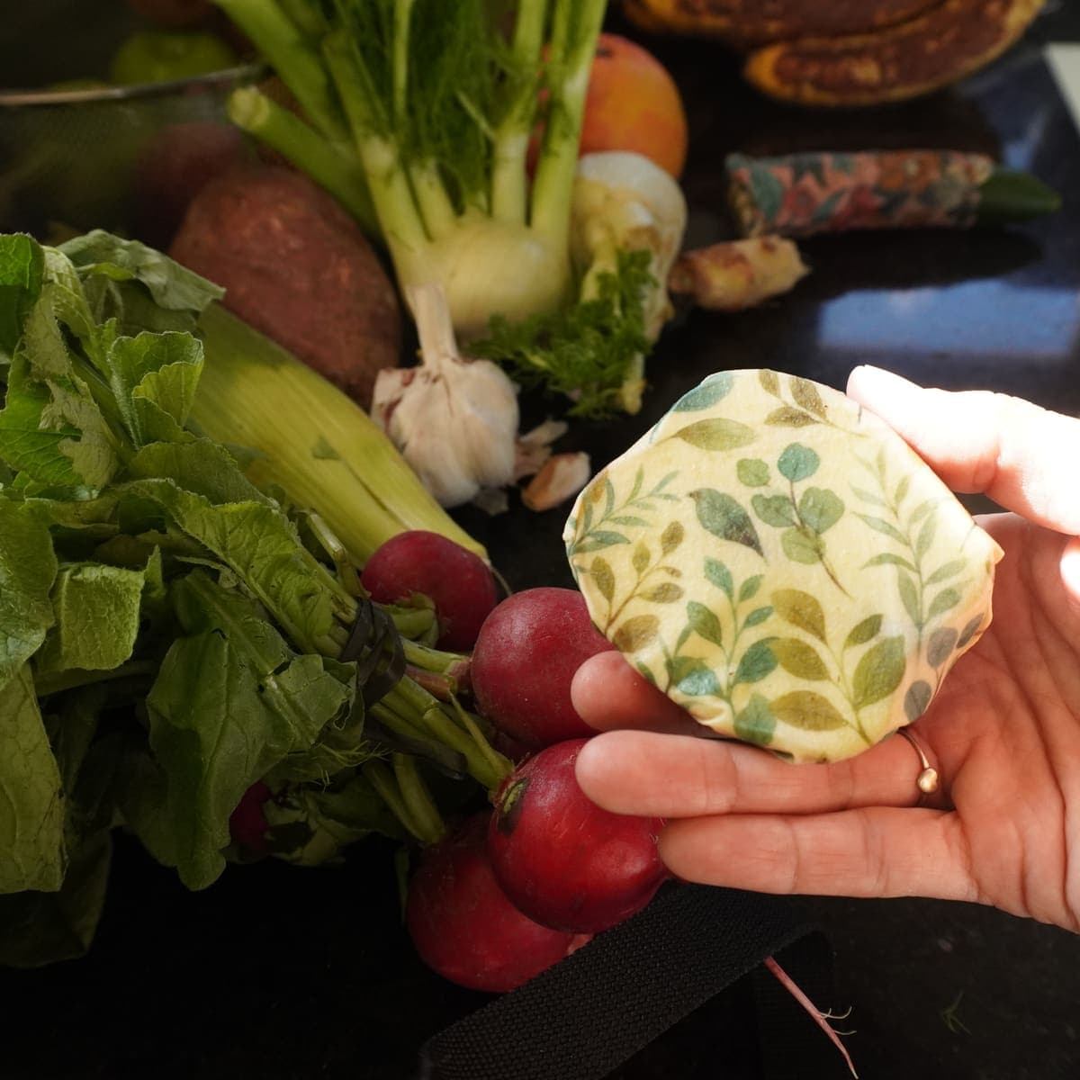Wrap de cera de abeja en la mano con verduras frescas detrás